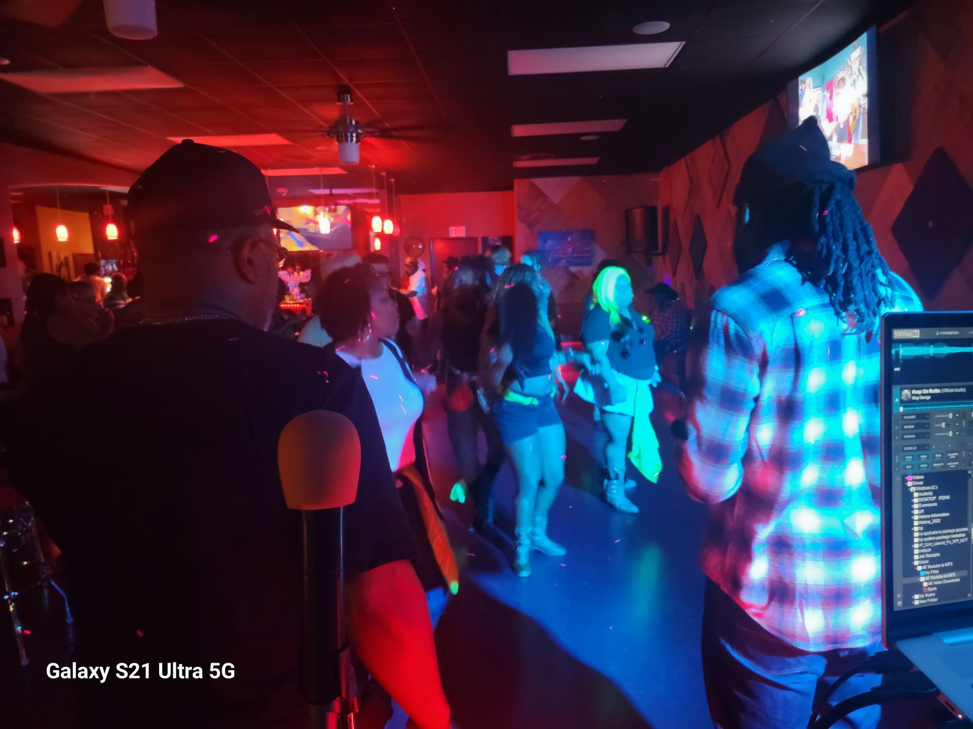 People dancing at a dimly lit bar. Red and blue lights illuminate the crowd. A DJ is in the foreground.