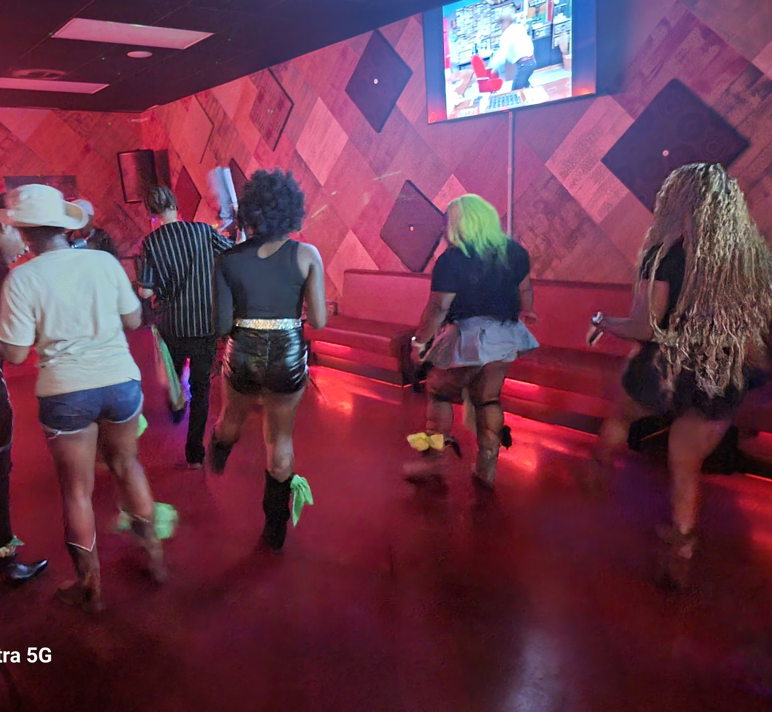 People line dancing in a dimly lit club with red walls.