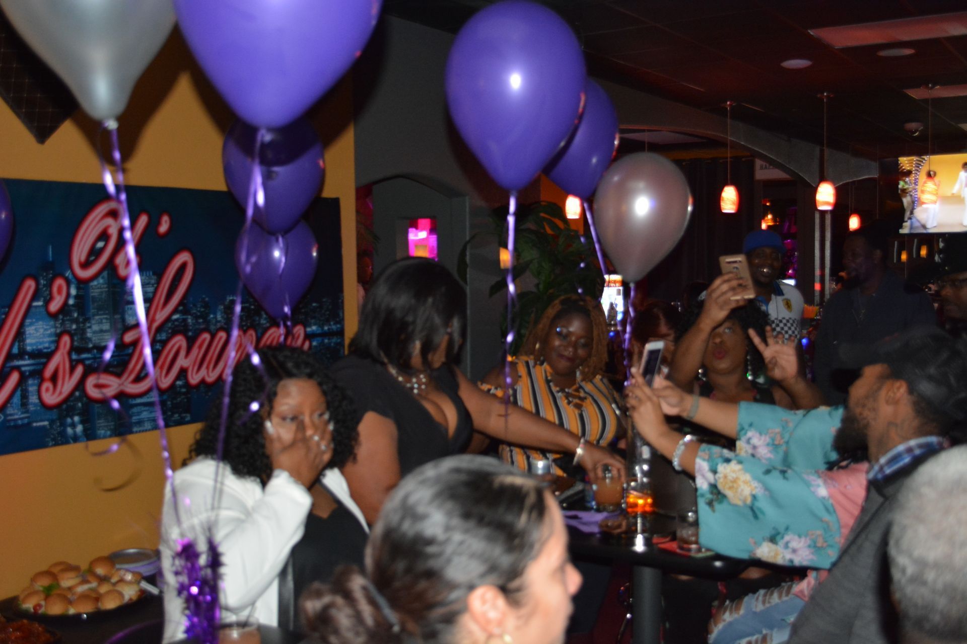 A group of people are gathered in a room with purple balloons