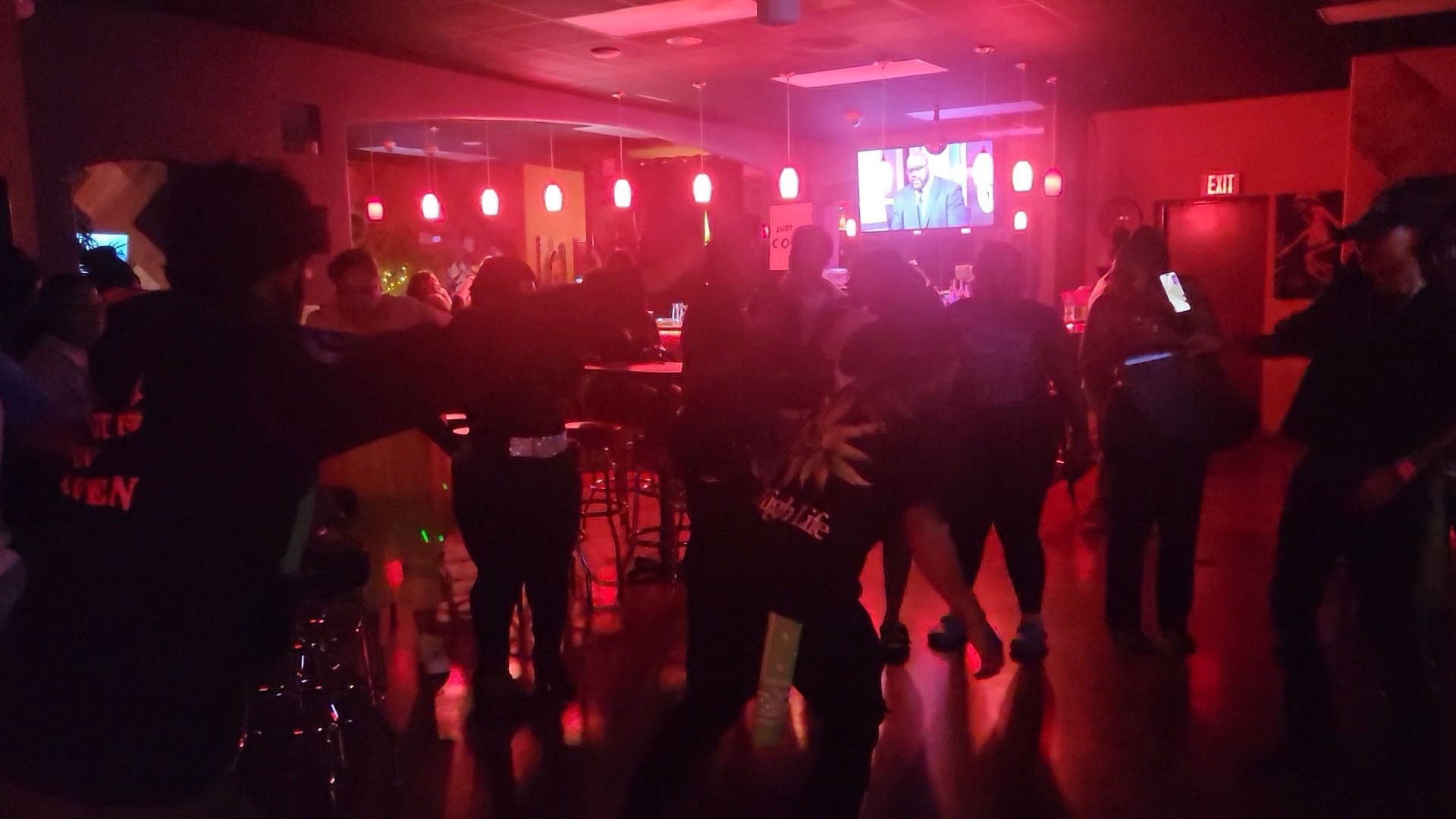 People dancing in a dimly lit bar with red lighting; silhouettes and shadows.