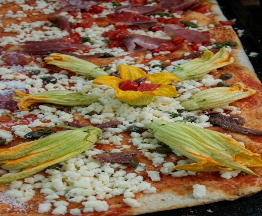 Pizza rettangolare con salsa di pomodoro, formaggio e fiori di zucchina gialla, cotta in una teglia da forno
