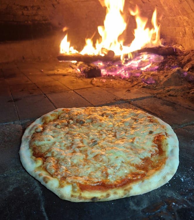Pizza al formaggio che cuoce sulla base in pietra del forno, con le fiamme sullo sfondo