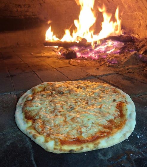 Pizza al formaggio che cuoce sulla base in pietra del forno, con le fiamme sullo sfondo