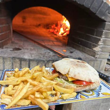 Pizza e patatine fritte su un piatto di ceramica davanti a un forno a legna