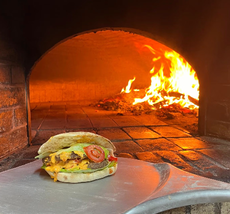 Panino pizza su una pala davanti a un forno a legna fiammeggiante