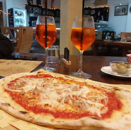 Pizza e due bibite all’arancia su un tavolo del ristorante, con una sala da pranzo accogliente sullo sfondo