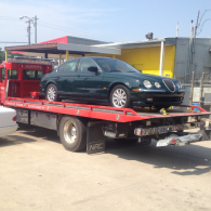 Black sedan loaded on a red tow truck in an industrial lot