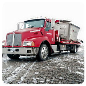 Red semi-truck hauling a silver trailer on a snowy, muddy road