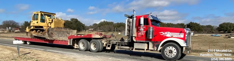 Red semi truck hauling a yellow bulldozer on a flatbed trailer in an open field