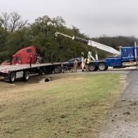 Tow truck lifting a red semi-truck from a roadside ditch on a cloudy day