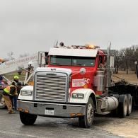 Red semi-truck at a construction site with workers and equipment nearby