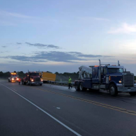 Tow trucks and workers on a highway shoulder at dusk after a roadside incident