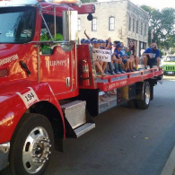 Red flatbed truck carrying seated people in a street parade