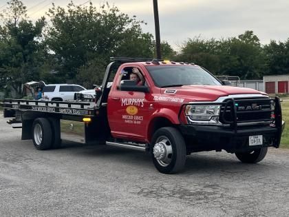 Red tow truck with flatbed parked outdoors near trees on an overcast day.