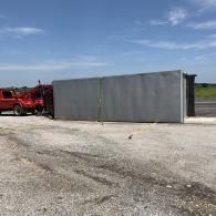 Red truck beside a long gray metal fence on a gravel lot under a blue sky