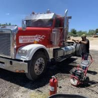 Red semi truck parked while a person works beside it with tools and a fire extinguisher nearby