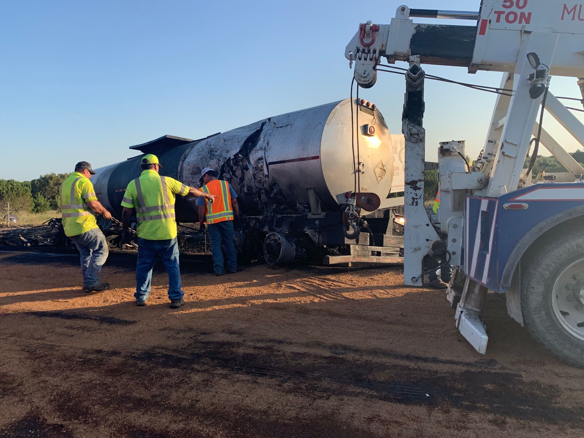 Workers in hi-vis gear and a tow truck clear a fuel tanker rollover on a roadside.