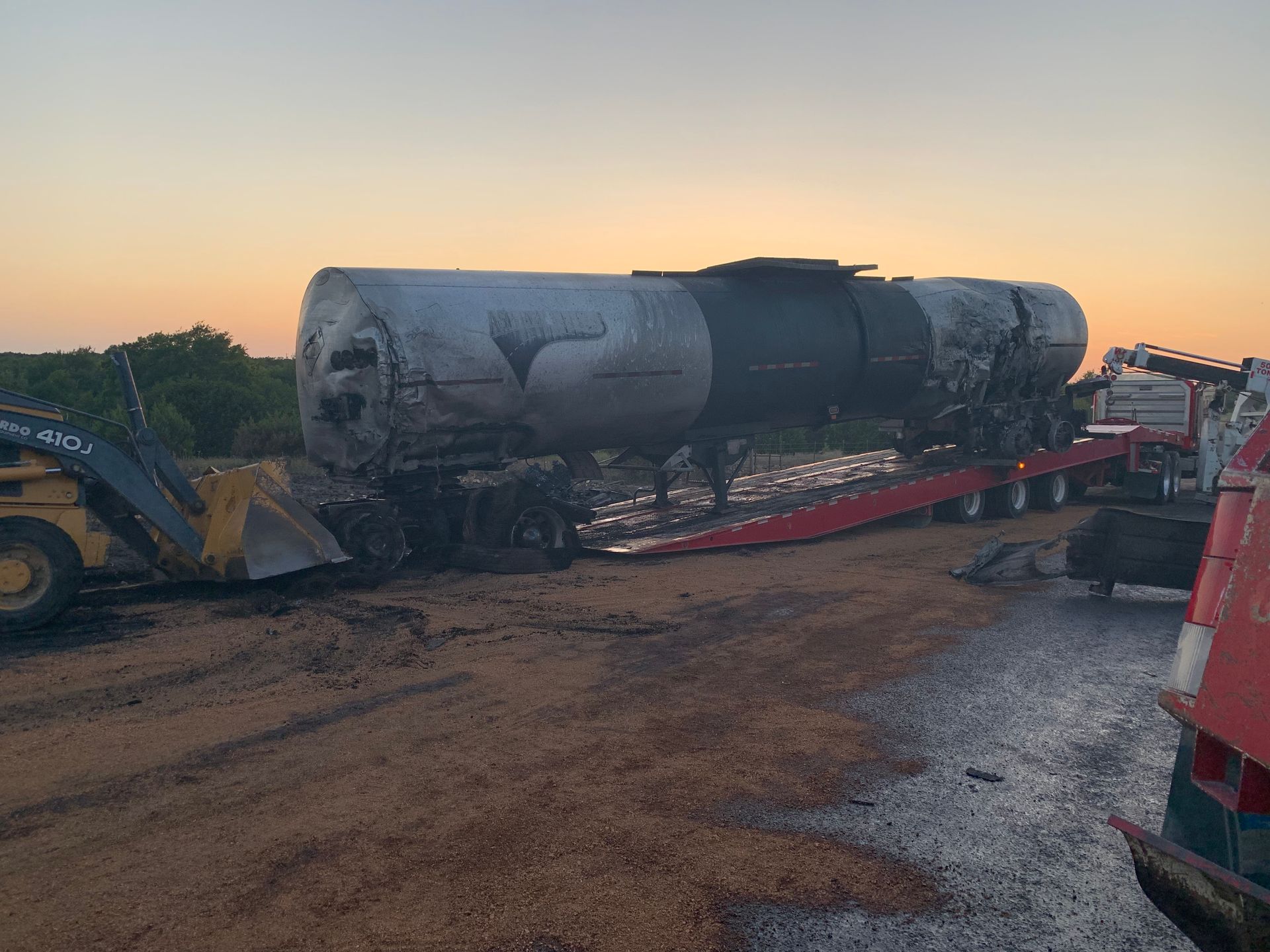 Large cylindrical tank on a red trailer at a construction site at sunset, with heavy machinery nearby