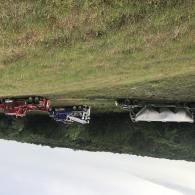 Upside-down view of a grassy field with a red truck, blue machinery, and a white tarp-covered trailer.