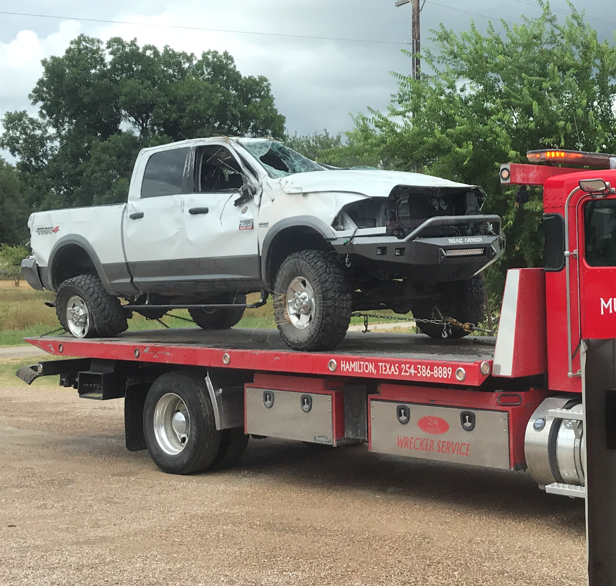 White pickup truck with front-end damage on a red tow truck in a parking lot