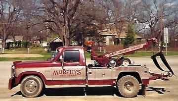 Red Murphy’s tow truck parked on a street in a neighborhood, with a tow arm extended.