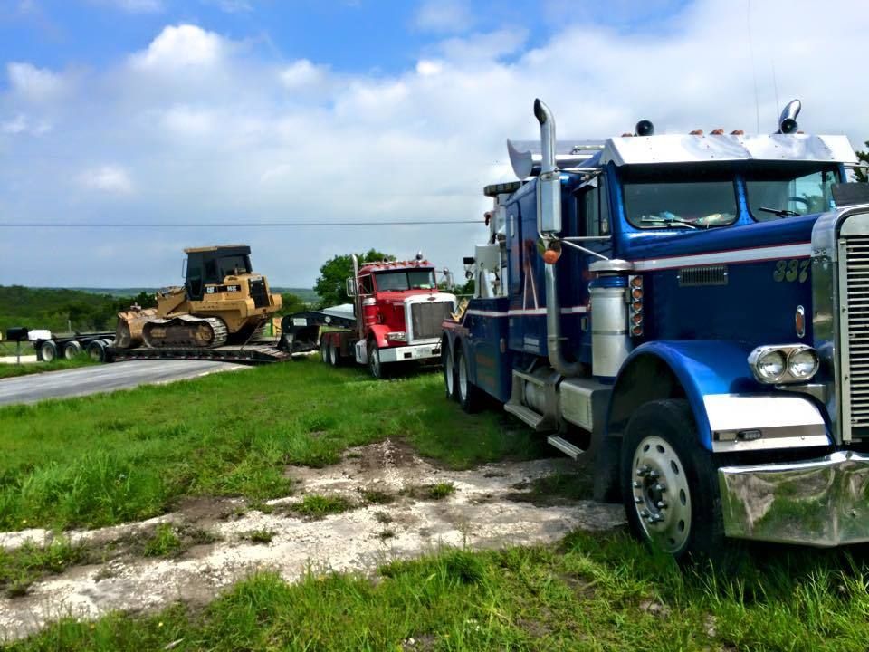 Blue semi truck on roadside with tow trucks and a bulldozer under a cloudy sky