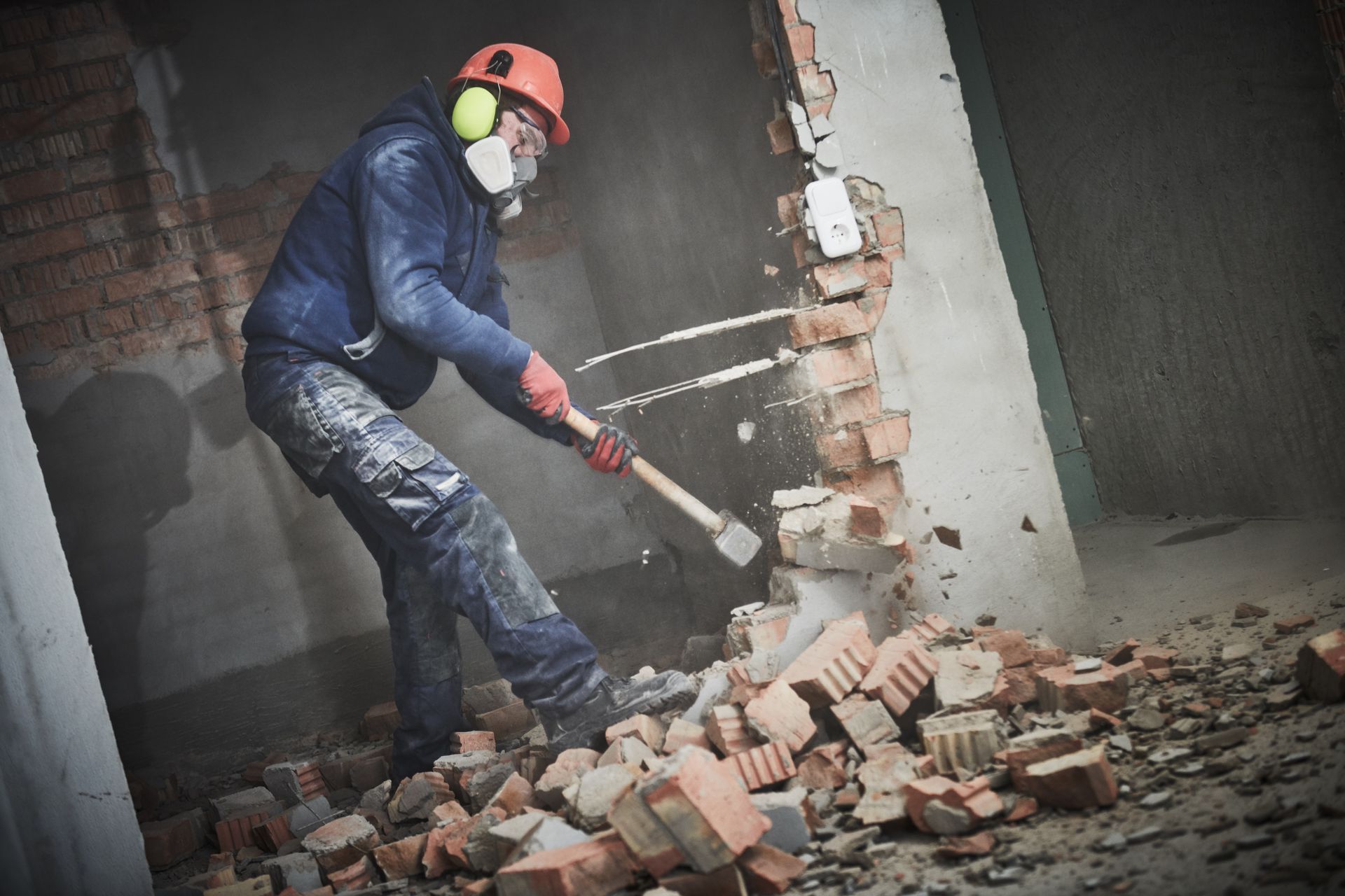 A man is breaking a brick wall with a hammer.