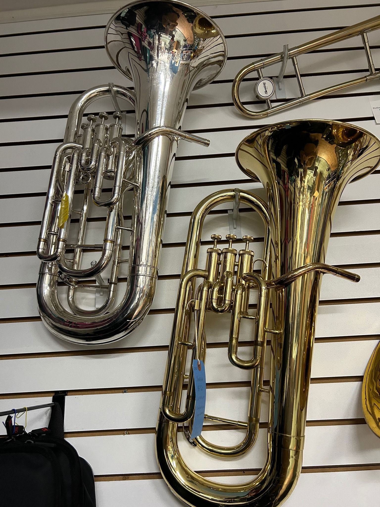 Silver and gold euphoniums displayed on a slatted wall.
