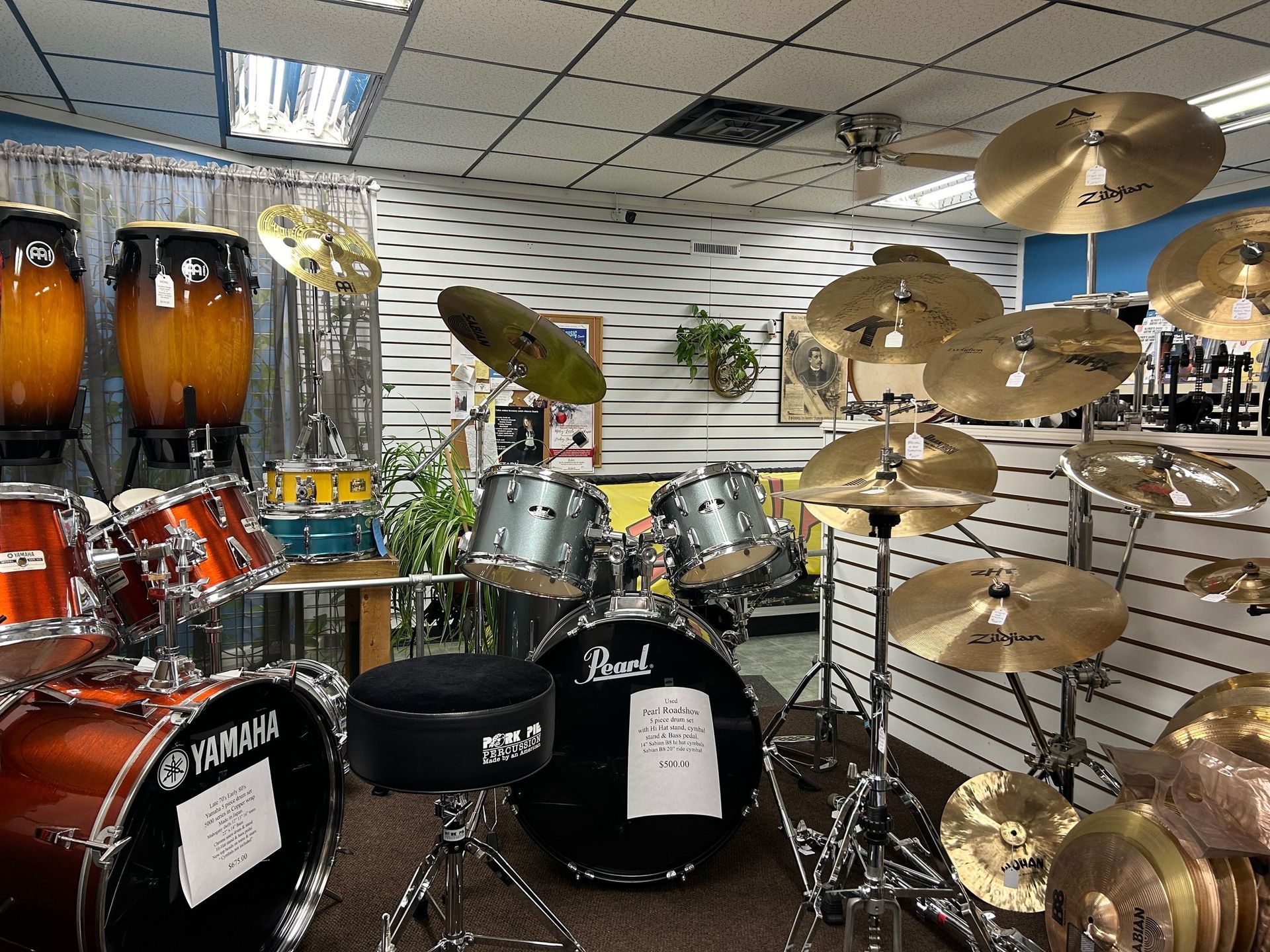 Drum sets and cymbals on display in a music store, with various brands and sizes visible.