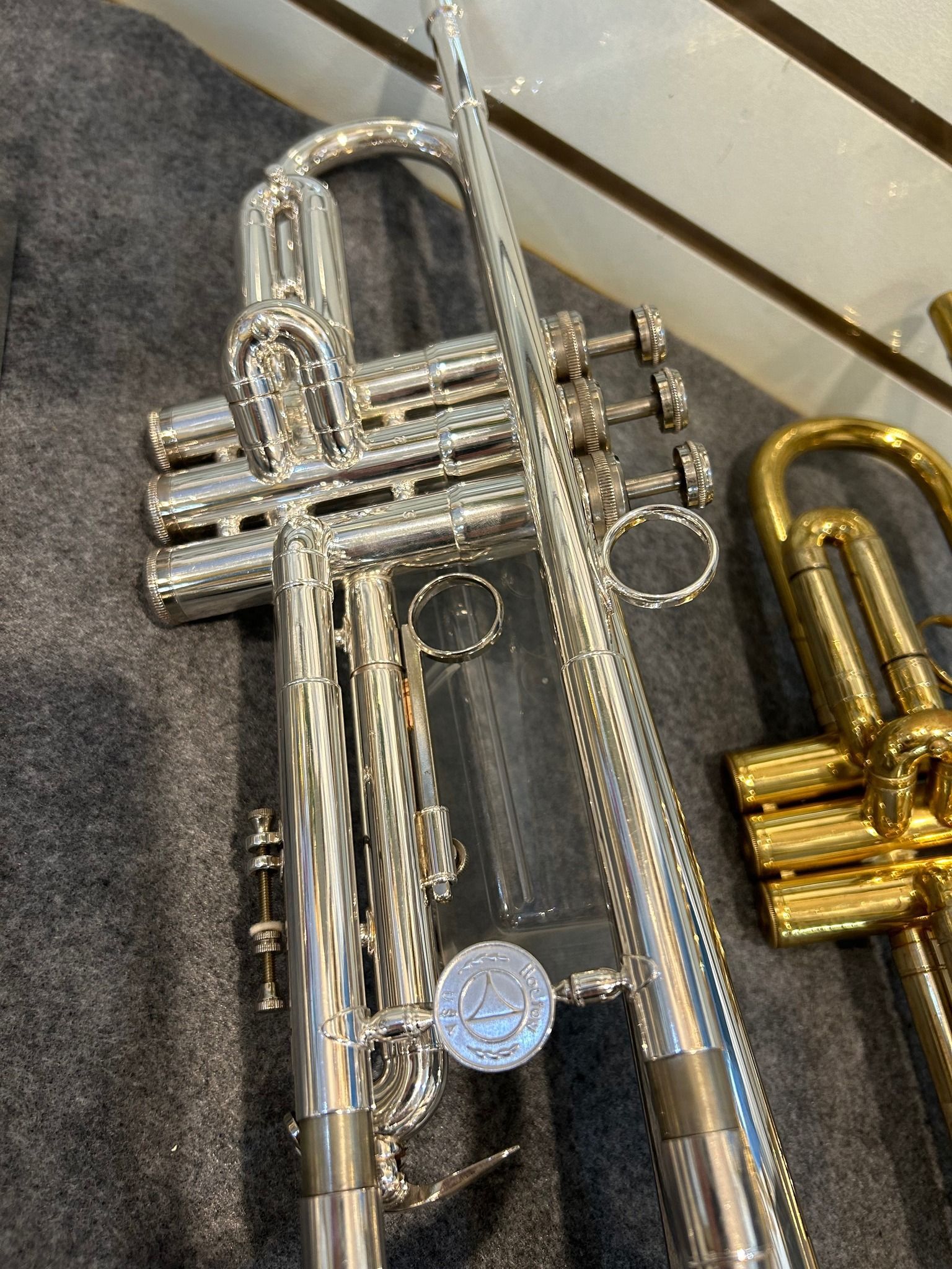 Silver trumpet resting on a gray surface, with a gold trumpet visible in the background.