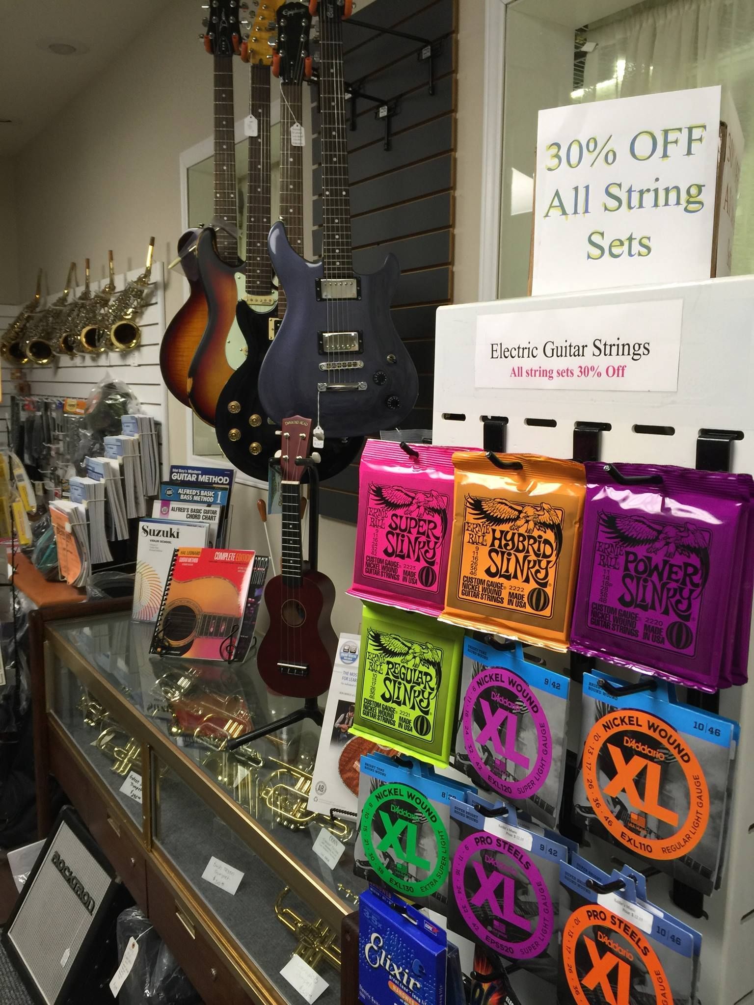 A guitar store display: Guitars, strings, and a sign advertising 30% off string sets.
