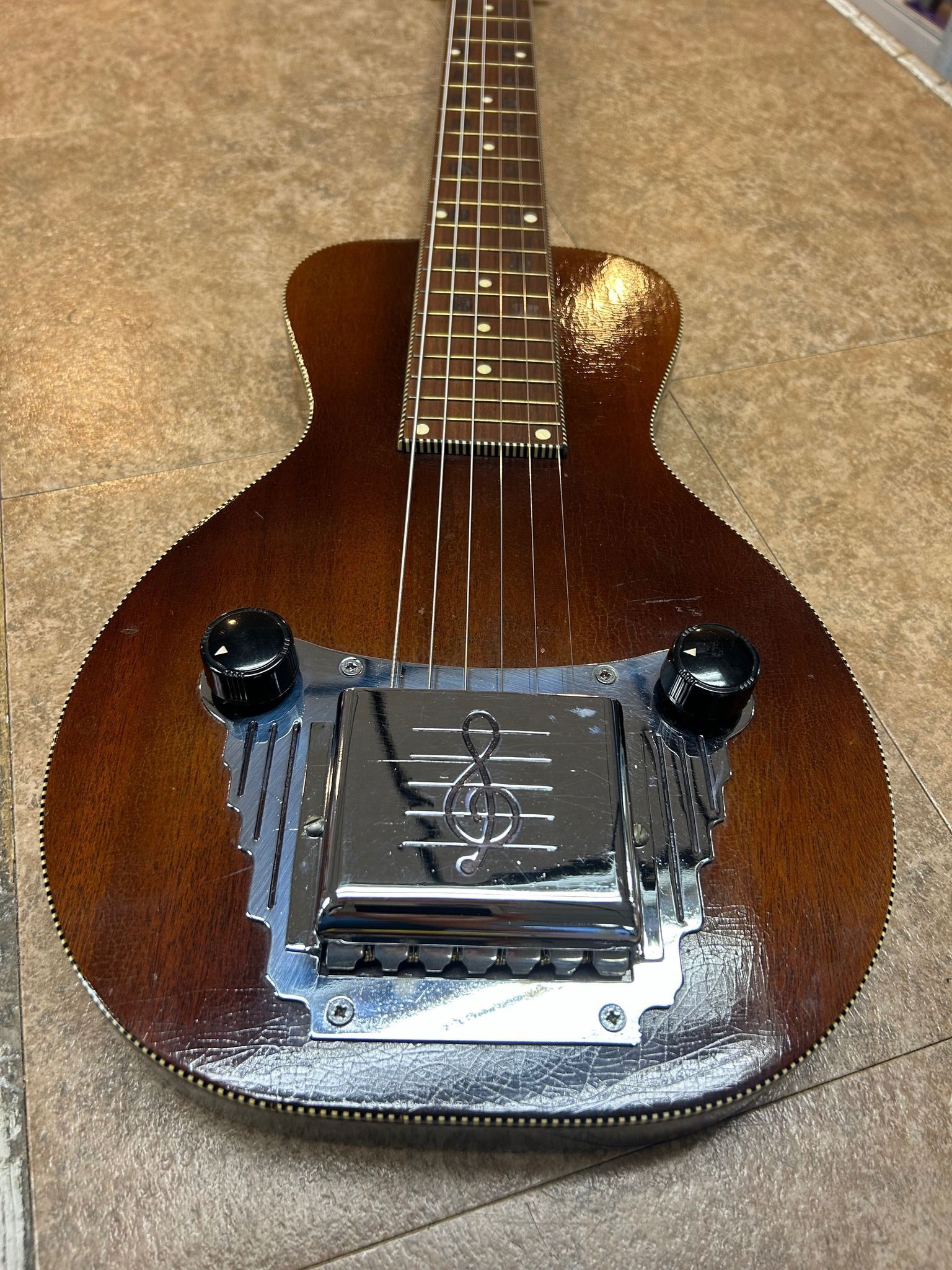 Brown electric lap steel guitar with silver hardware and black knobs on a textured surface.