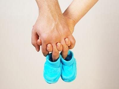 Adult hands holding a child’s hands, with blue baby shoes hanging below.