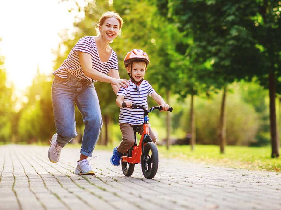Adult helping child ride a small bike on a sunlit park path