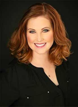 Smiling woman with shoulder-length auburn hair wearing a black blouse against a dark background