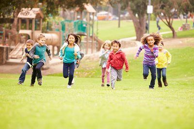 Children running together on a grassy field in a park, smiling and playing outdoors.