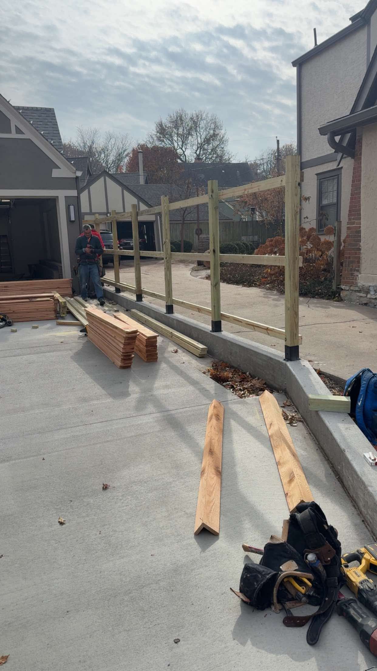 Construction of a wooden fence along a concrete wall near a house. A worker is using tools.