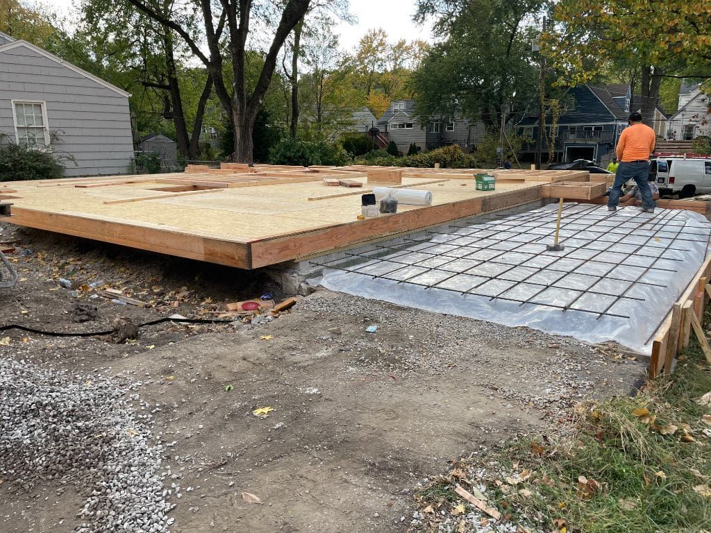 A man is standing on a concrete slab in front of a house under construction.