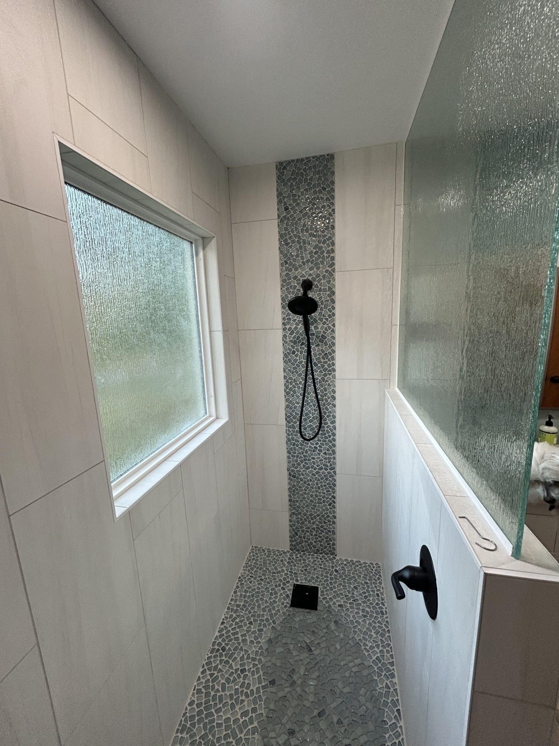 A bathroom with a walk in shower and a window.