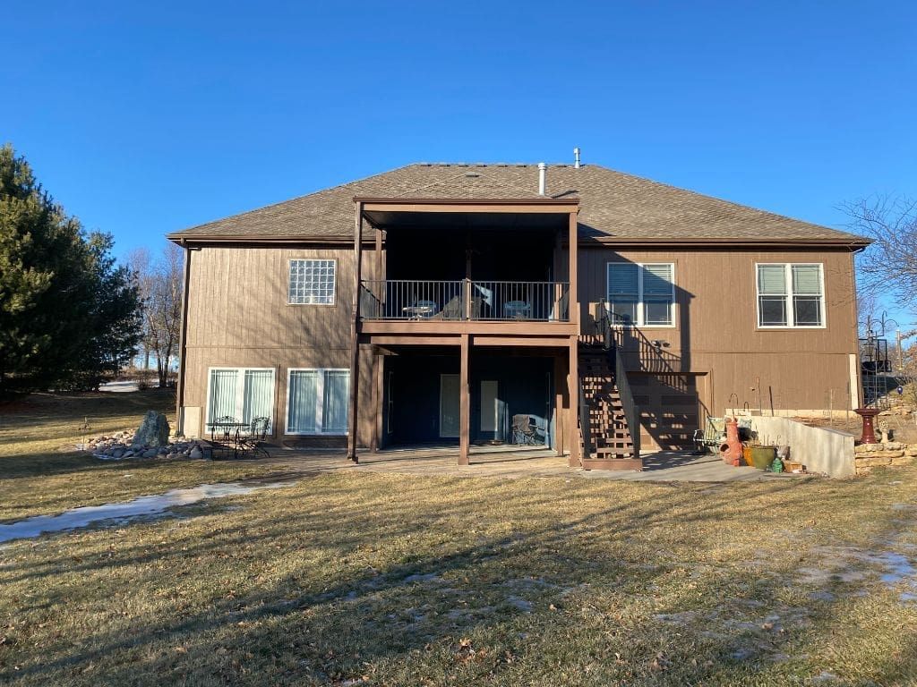 The back of a large house with a large deck and stairs.