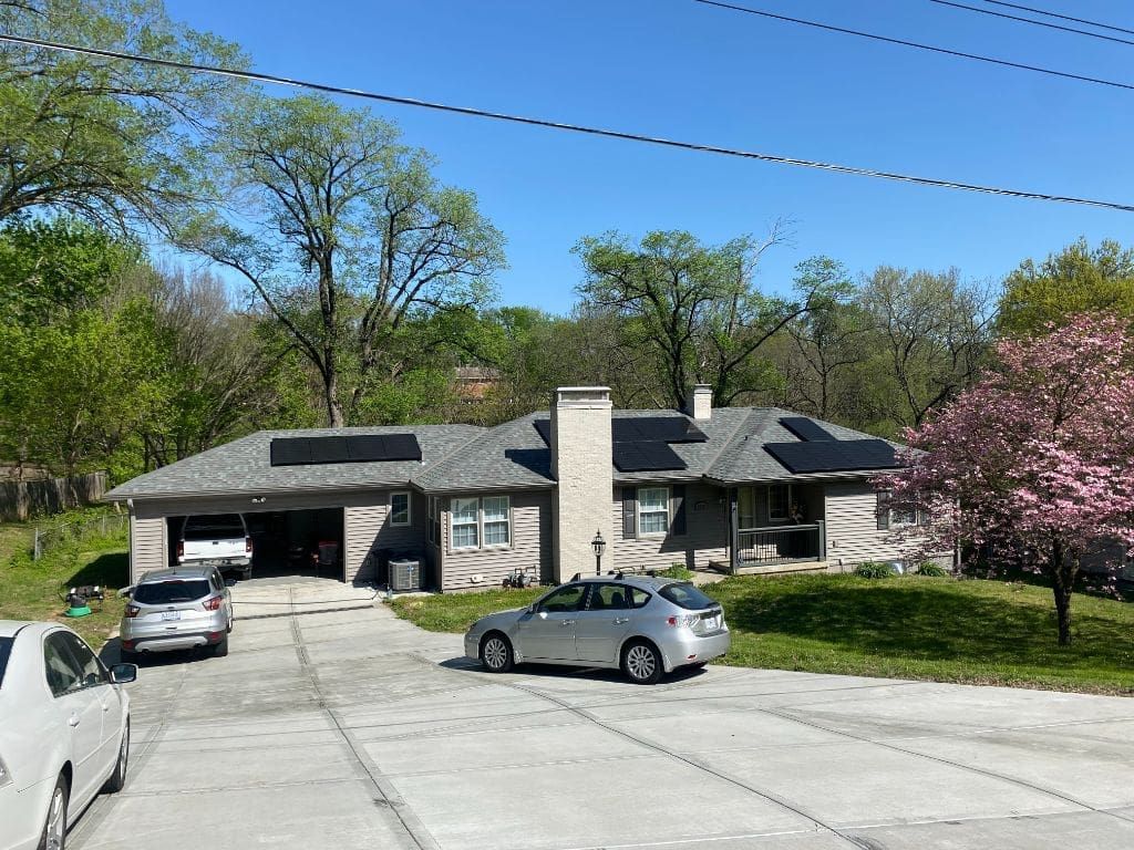 A car is parked in front of a house with solar panels on the roof.