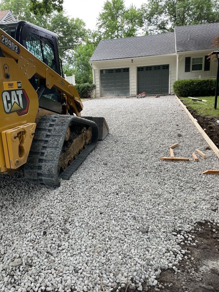 A bulldozer is working on a gravel driveway in front of a house.