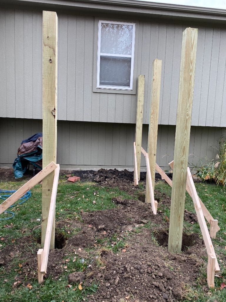 A row of wooden posts sitting in the dirt in front of a house.