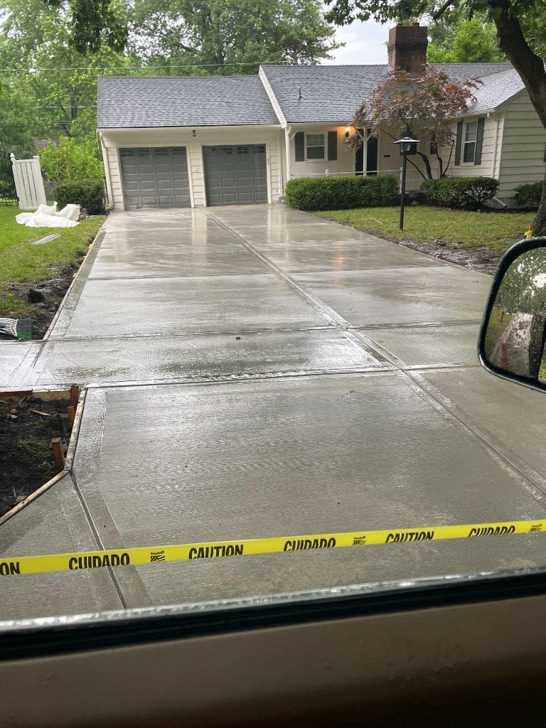 A car is driving down a concrete driveway in front of a house.
