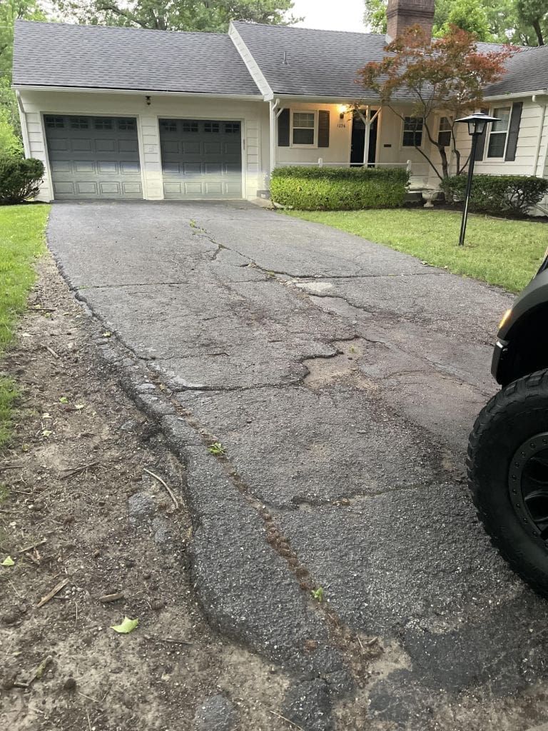 A car is parked in front of a house with a cracked driveway.