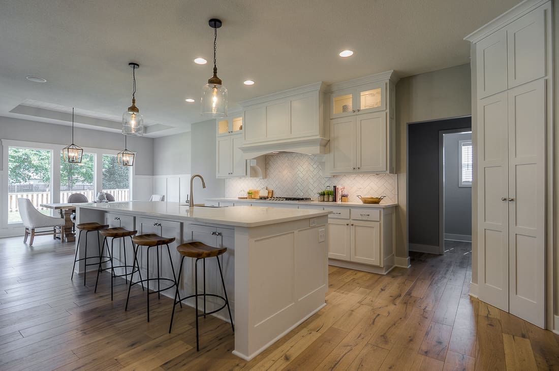 A kitchen with white cabinets , a large island , and wooden floors.