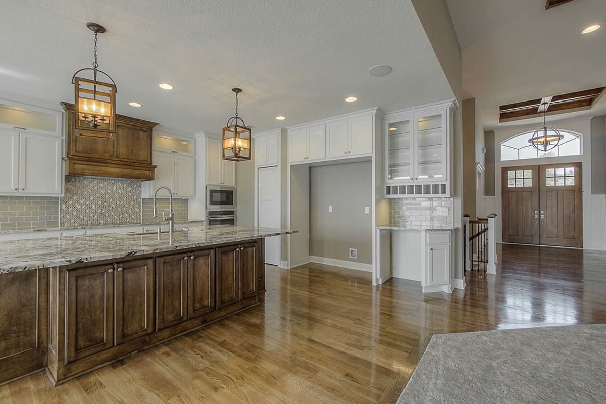 A kitchen with hardwood floors , white cabinets , granite counter tops and a large island.