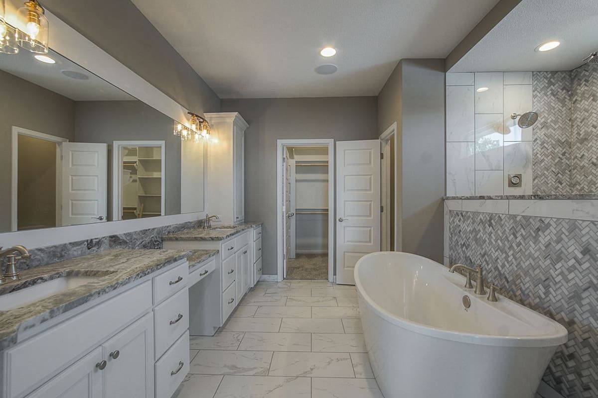 A bathroom with a tub , sinks , mirrors and a walk in closet.