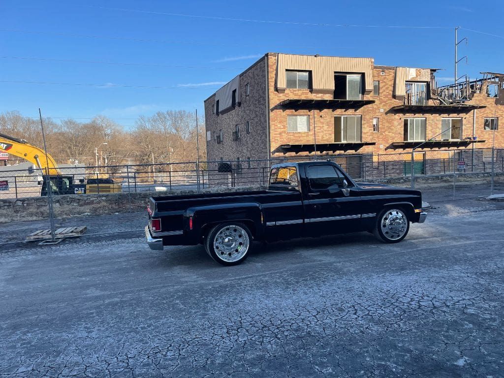 A black truck is parked in a gravel lot in front of a brick building.
