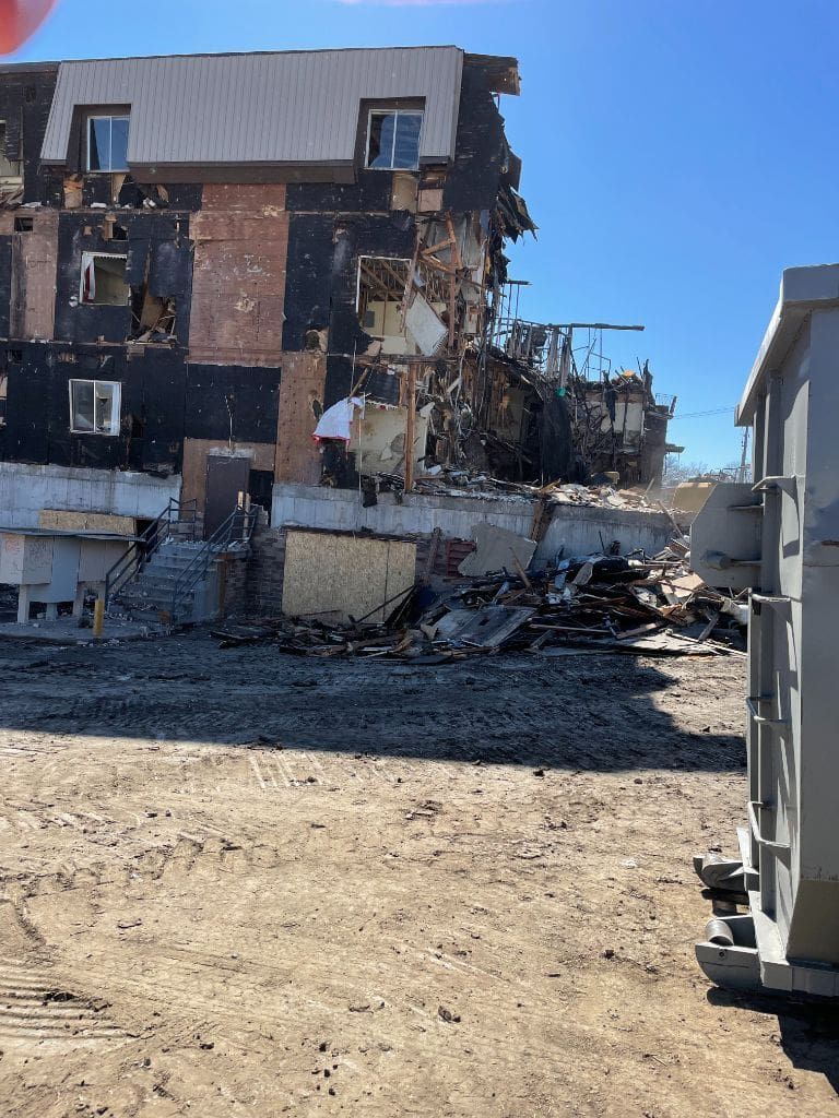 A large building is being demolished in the middle of a dirt field.